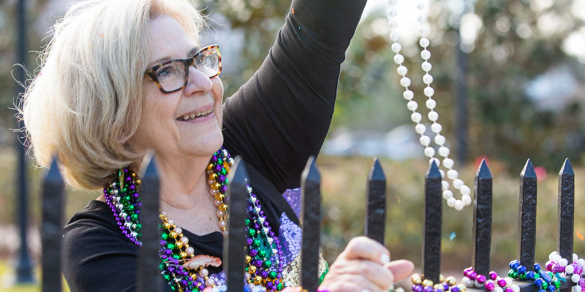 Smiling senior woman in glasses catching Mardi Gras beads along a fence at an independent living community in New Orleans
